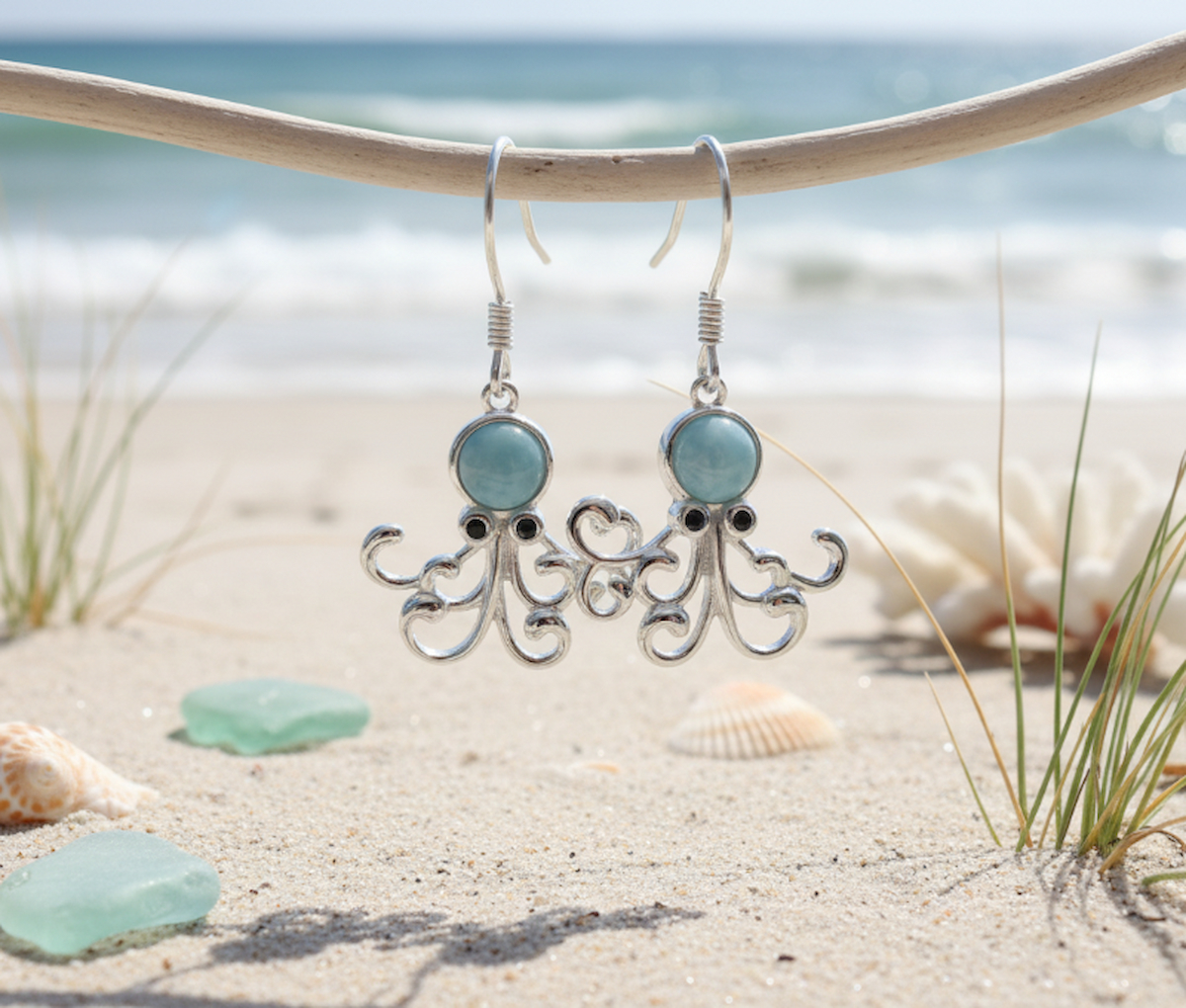Sterling silver Larimar octopus earrings hanging on driftwood at the beach