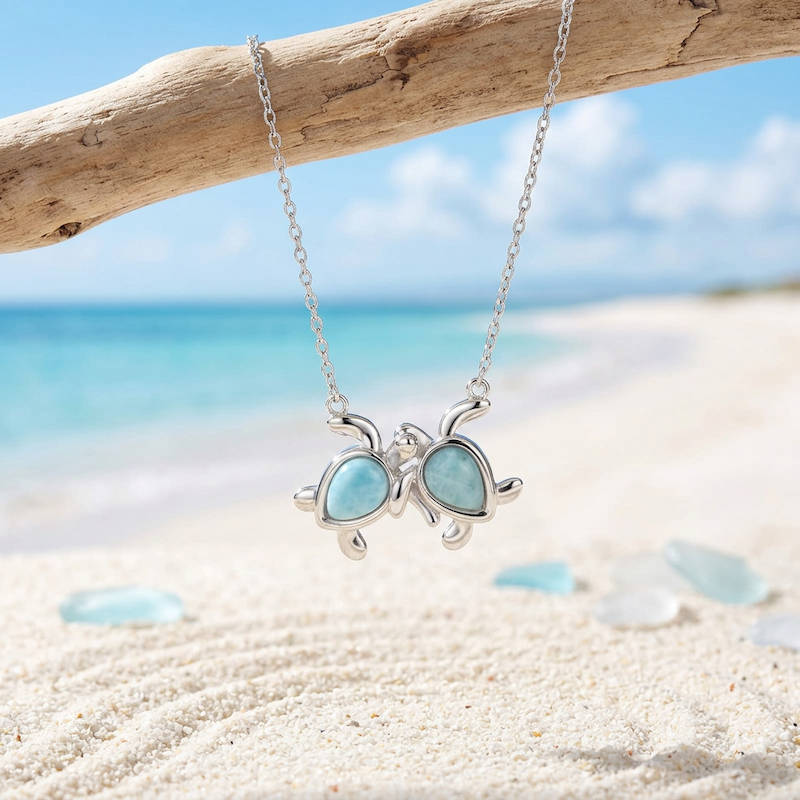 Larimar Two Turtle Necklace in Sterling Silver hanging on driftwood at the beach