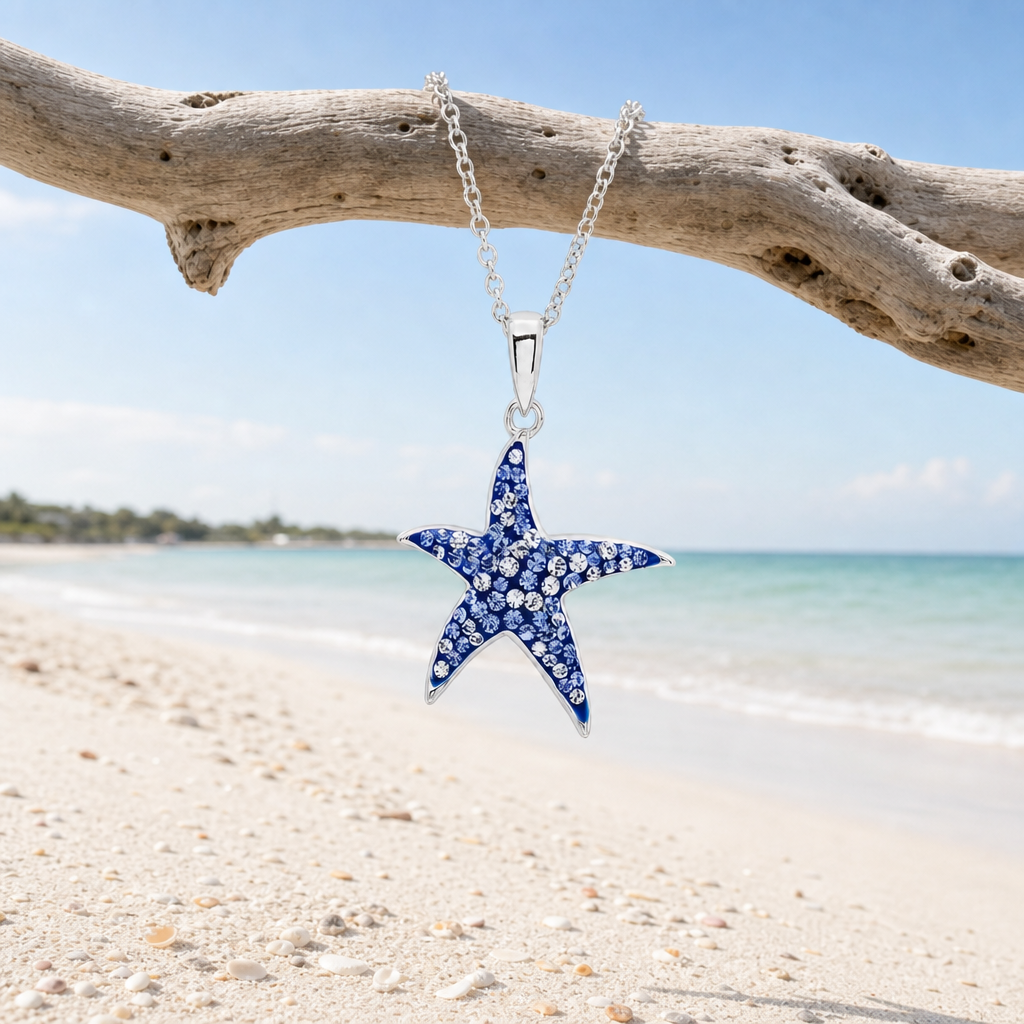 Sterling silver sapphire blue starfish necklace with crystal accents hanging from driftwood on Florida Gulf Coast beach &mdash; Crabby Mermaid