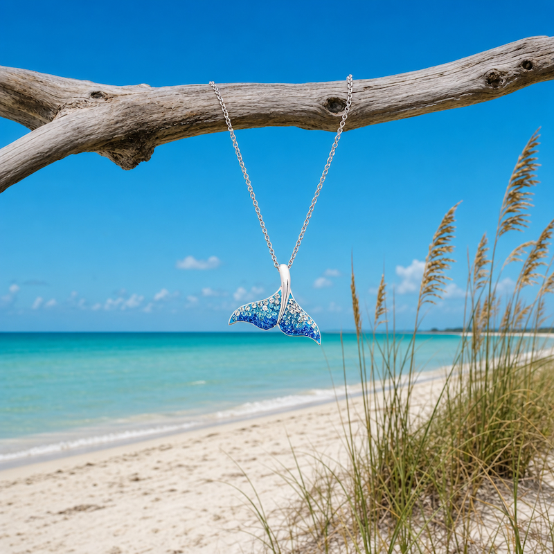 Sterling Silver Whale Tail Necklace with Ombre Blue Crystals on driftwood at the beach